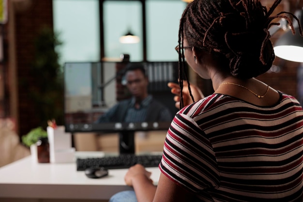 ビデオ会議で従業員と話している女性、自宅で働くアフリカ系アメリカ人のフリーランサー。リモート ワーカーが仮想会議に参加し、コンピューターを使用して電話会議でチャットする
