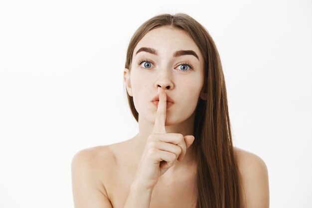 woman telling secret and making shh sigh, showing shush gesture with index finger over mouth