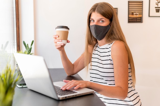 Woman at terrace with laptop wearing mask