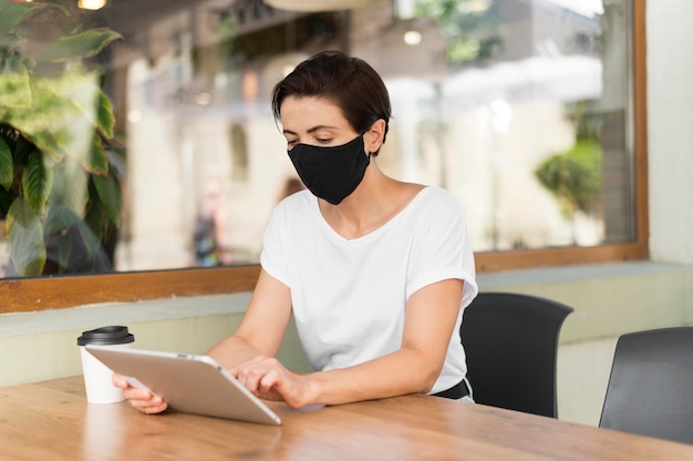 Woman at terrace with tablet wearing mask