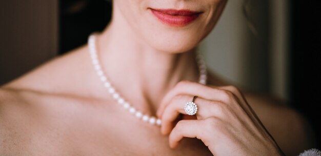 女性は彼女の首に柔らかい真珠のネックレスに触れる