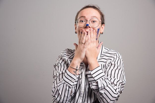 Woman touching her face with her paints hands on gray background