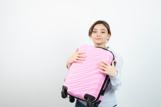 Женщина-туристка стоит и держит розовый чемодан. Фото высокого качества