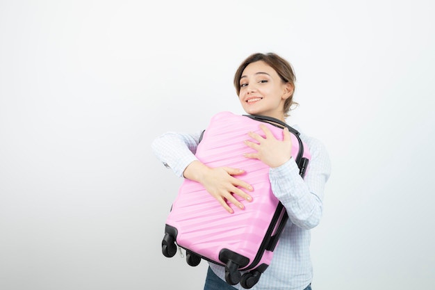 Woman tourist standing and hugging pink travel suitcase . High quality photo