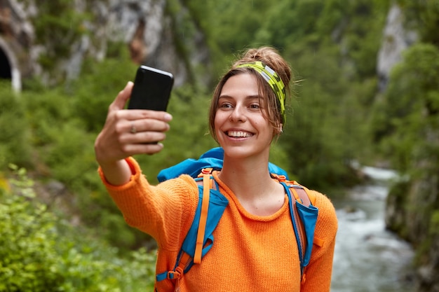 女性観光客はスマートフォンで自分の写真を撮り、山で忘れられない旅をし、小川に立ち向かう