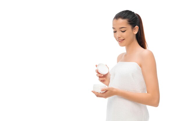 Woman in towel holding cosmetic product on white