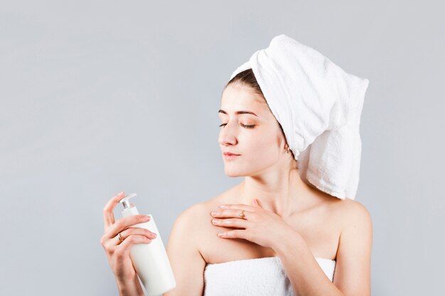 Woman in towels holding cosmetic bottle