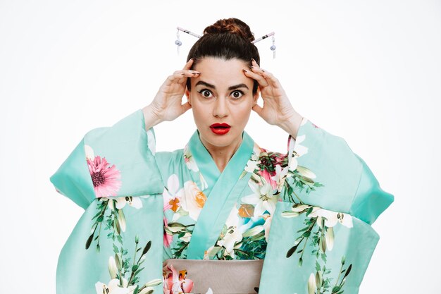 Woman in traditional japanese kimono being shocked raising hands touching temples on white