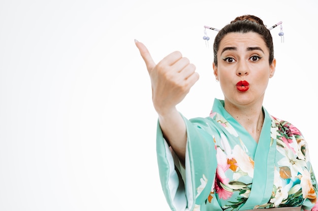 Free photo woman in traditional japanese kimono emotionally pointing with thumb to the side on white