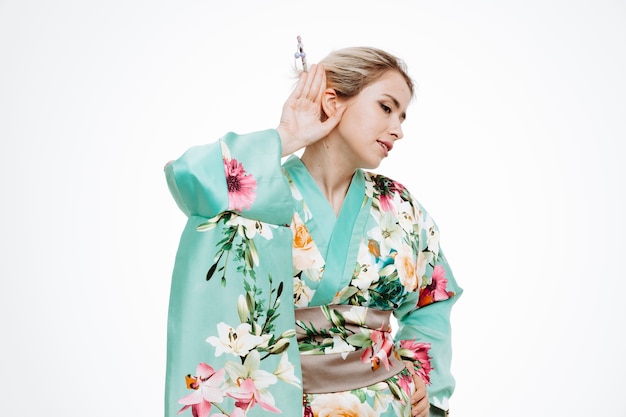 Woman in traditional japanese kimono holding hand on ear trying to listen to gossip on white