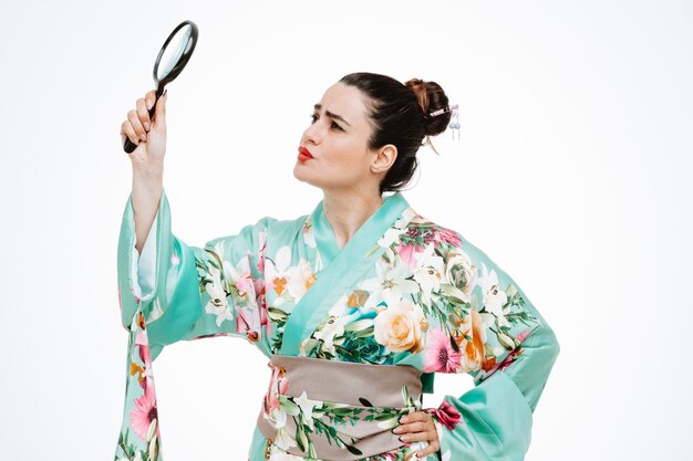 Woman in traditional japanese kimono holding magnifying glass looking at it being intrigued on white