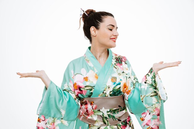 Woman in traditional japanese kimono looking aside presenting something with arms of her hands on white