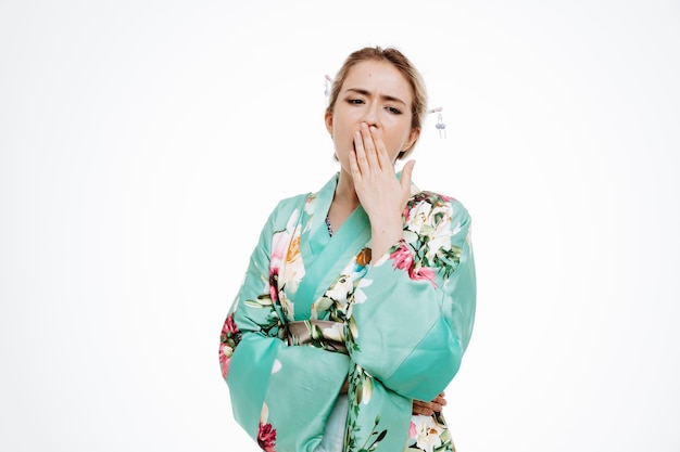 Woman in traditional japanese kimono looking tired and bored yawning holding hand on mouth on white