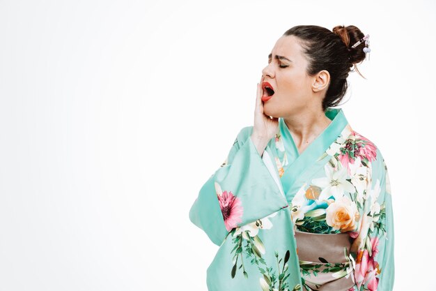 Woman in traditional japanese kimono looking unwell touching her cheek feeling toothache on white