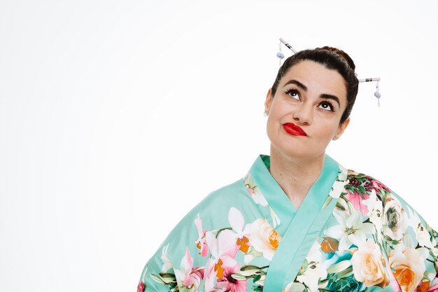 Woman in traditional japanese kimono looking up being displeased making wry mouth on white