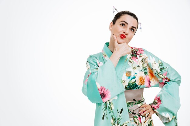 Woman in traditional japanese kimono looking up with pensive expression trying to make choice thinking on white