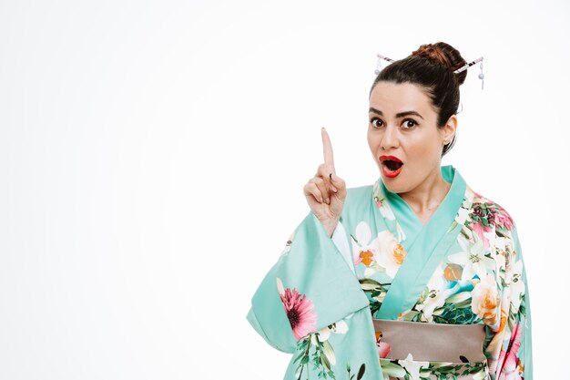 Woman in traditional japanese kimono surprised pointing with index finger up having new idea on white