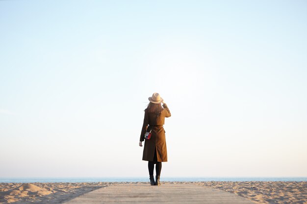 woman traveler enjoying view of calm sea in autumn or spring outwear looking into distance.