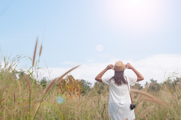 woman traveler with camera holding hat and breathing at field of grasses and forest, wanderlust travel concept, space for text, atmosperic epic moment