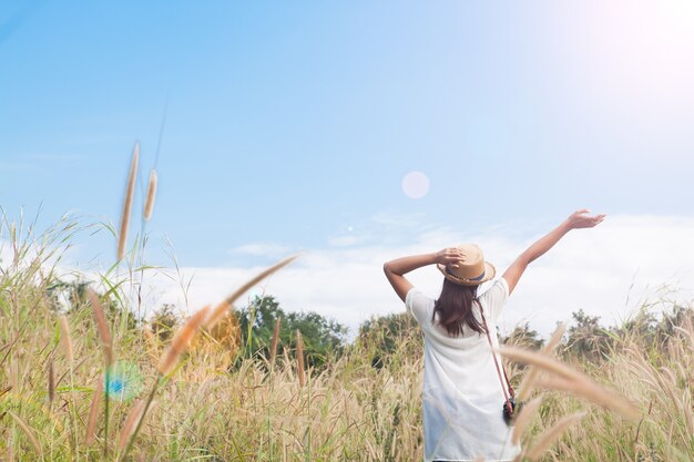 woman traveler with camera holding hat and breathing at field of grasses and forest, wanderlust travel concept, space for text, atmosperic epic moment