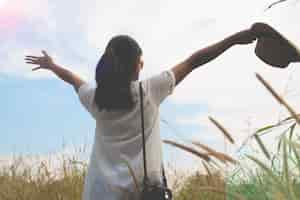 Free photo woman traveler with camera holding hat and breathing at field of yard and forest, wanderlust travel concept, space for text, atmosperic epic moment