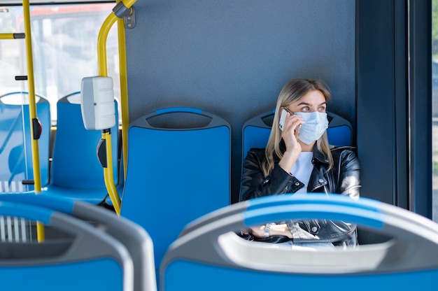 Woman traveling by public bus talking on the phone while wearing medical mask for protection