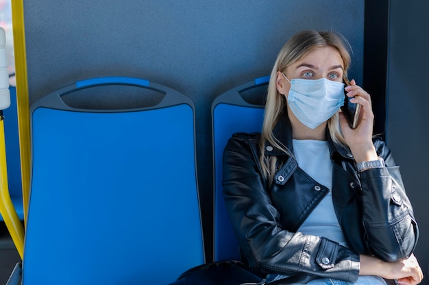 Woman traveling by public bus talking on the phone while wearing medical mask for protection
