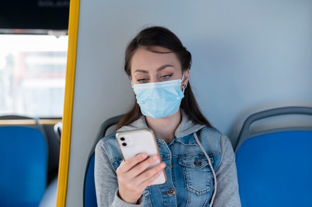 Woman traveling by public bus using smartphone while wearing medical mask for protection