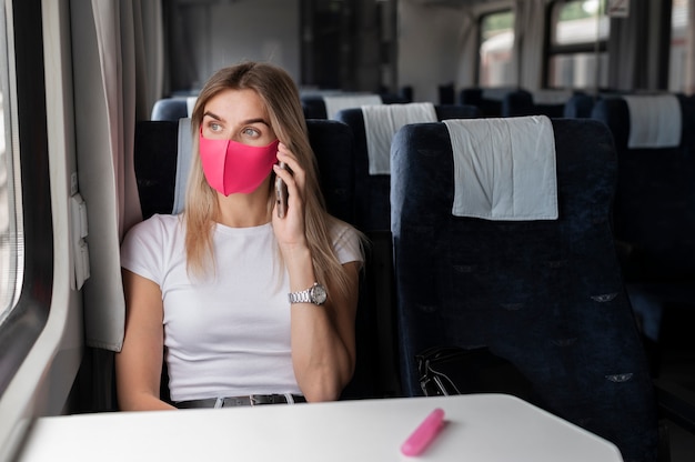 電車で旅行し、医療用マスクを着用して電話で話している女性