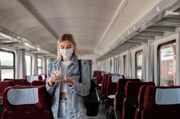 保護のために手指消毒剤スプレーを使用して電車で旅行している女性