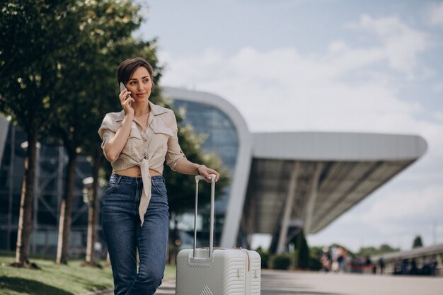 空港で荷物を持って旅行し、電話で話している女性