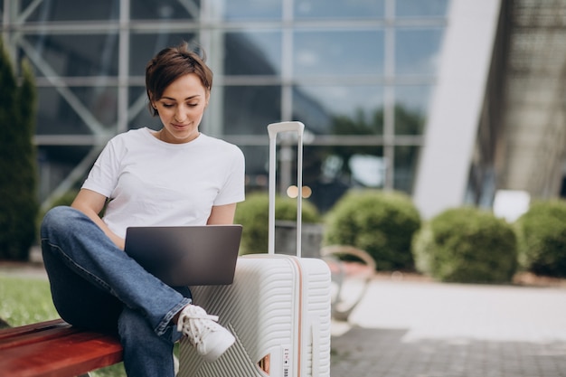 空港で旅行し、コンピューターで作業している女性