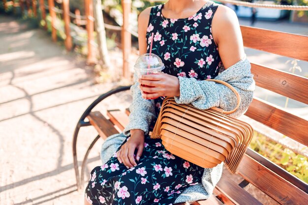 Woman in trendy cardigan sitting in the park and drinking smoothie