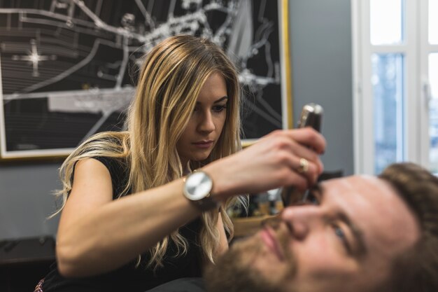 Woman trimming beard of client