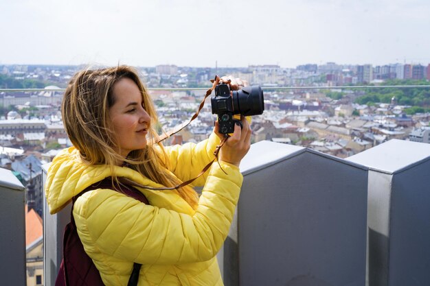 旅行中の女性が高所から街の写真を撮ります。カメラを持つ女性。女性写真家