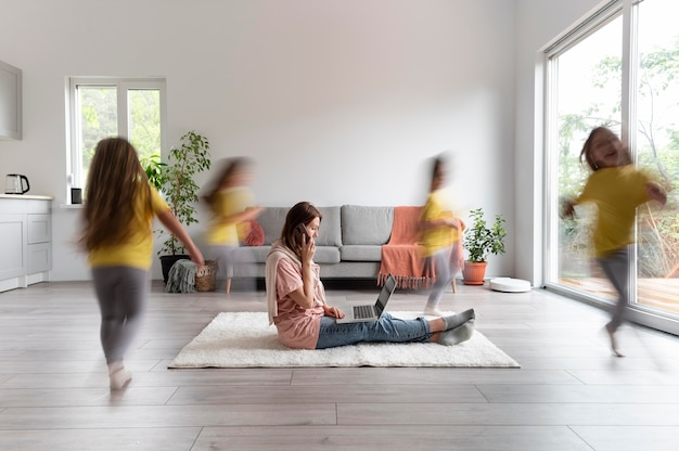 Woman trying to work on laptop from home while her children are running around