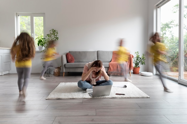 Foto gratuita donna che cerca di lavorare su un laptop da casa mentre i suoi figli corrono in giro