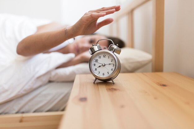 ベッドに横たわっている間に目覚まし時計を切っている女性