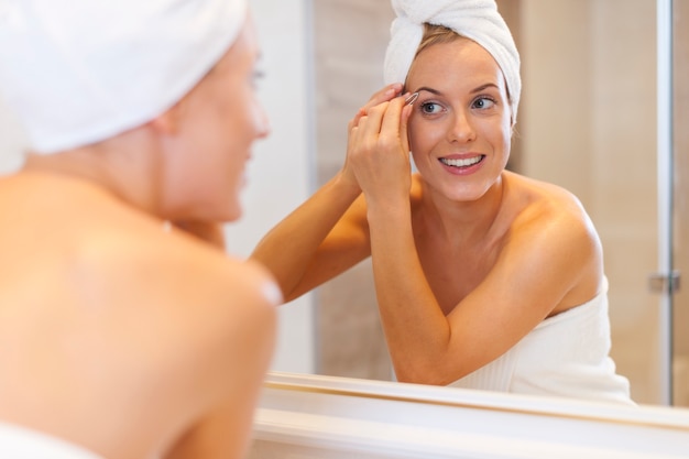 Free photo woman tweezing eyebrows in front of mirror