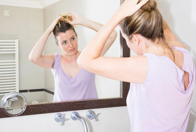Woman tying her hair looking at mirror in the bathroom