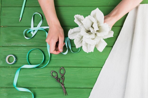 Woman tying paper flower with ribbon against wooden table