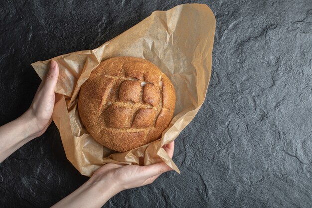 Woman unwrap freshly baked rye bread on black background.