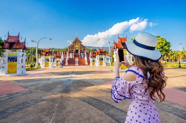 여자는 태국 치앙마이의 Royal Flora ratchaphruek에서 Ho kham luang 북부 태국 스타일에서 휴대 전화를 사용하여 사진을 찍습니다.