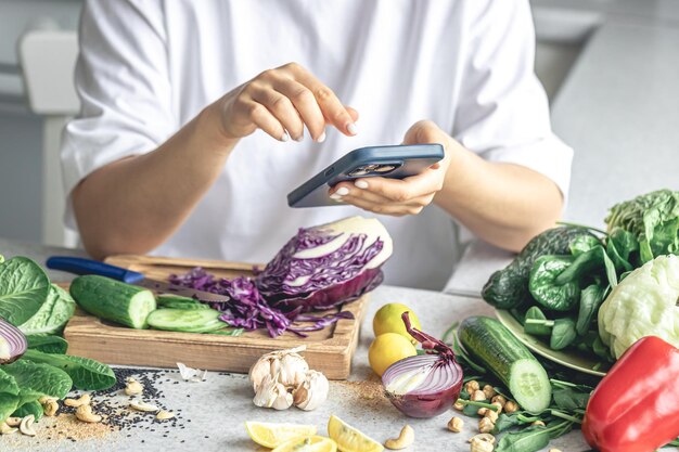 女性がキッチンでスマートフォンを使って野菜サラダを準備している