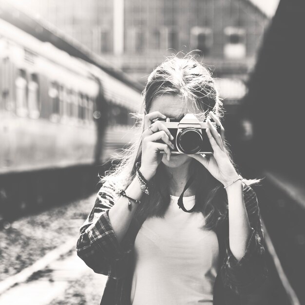 Женщина с помощью камеры, делающей фото на вокзале в оттенках серого