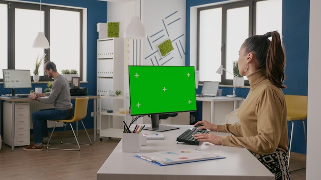 Woman using computer with isolated green screen at desk. Person working with chroma key and mock up copy space background on monitor for startup business. Blank chromakey template.