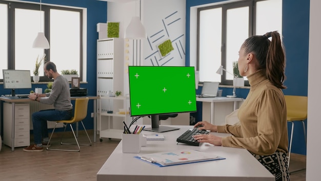 机の上の孤立した緑色の画面でコンピューターを使用している女性。クロマキーを操作し、スタートアップビジネスのモニターにコピースペースの背景をモックアップする人。空白のクロマキーテンプレート。