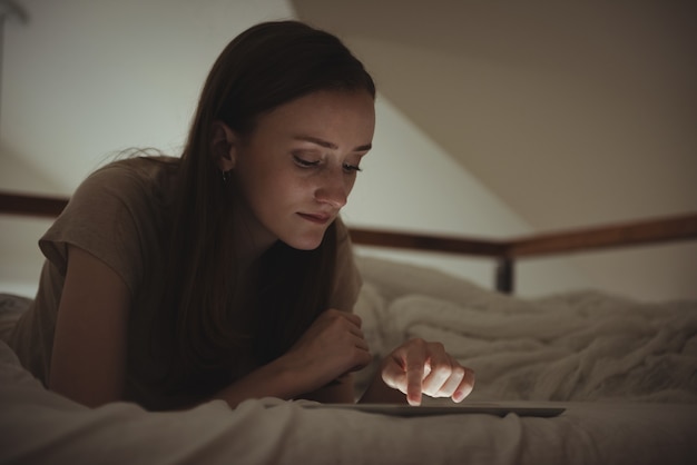 Женщина с помощью цифрового планшета на кровати