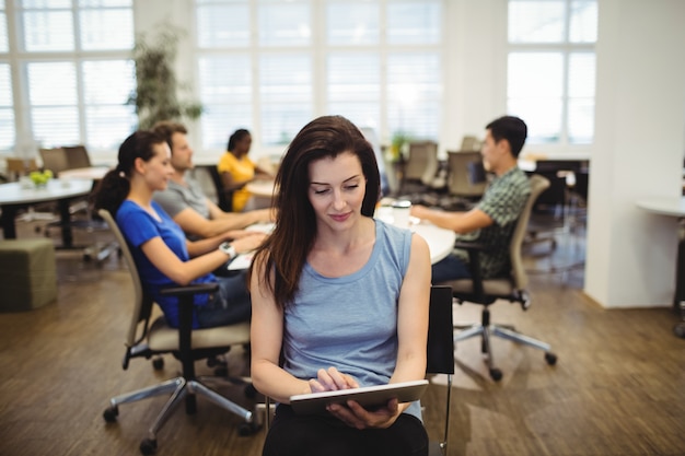 Woman using digital tablet while colleagues working in backgroun