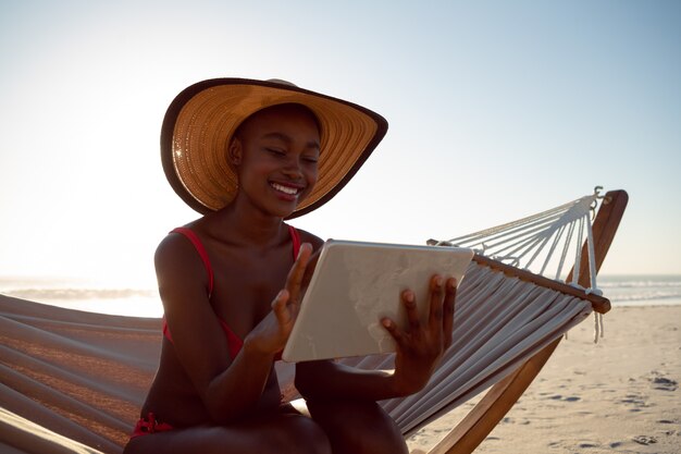 해변에서 해먹에서 휴식을 취하는 동안 디지털 태블릿을 사용하는 여자
